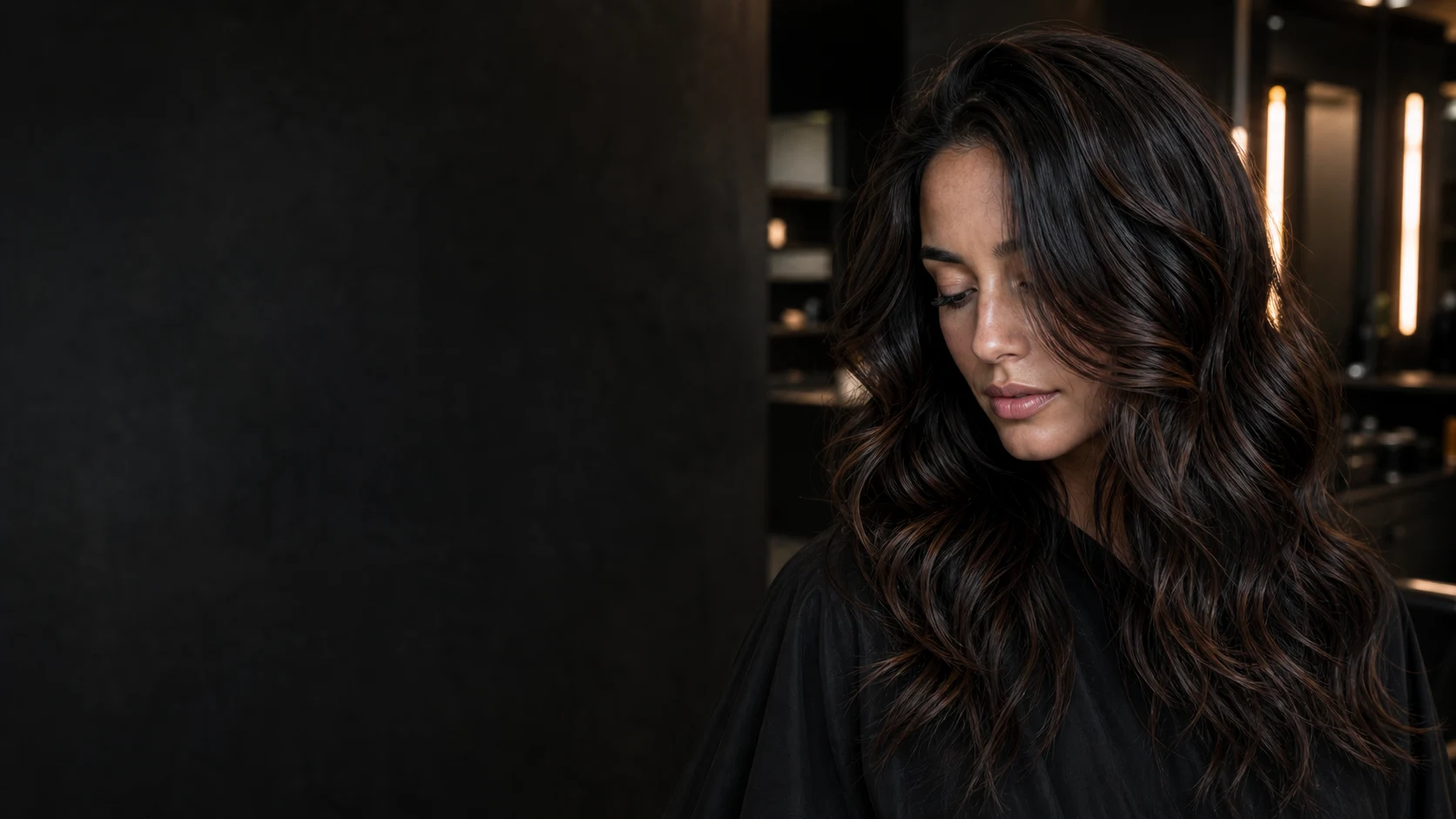 Client with glossy brunette waves in a softly lit modern salon